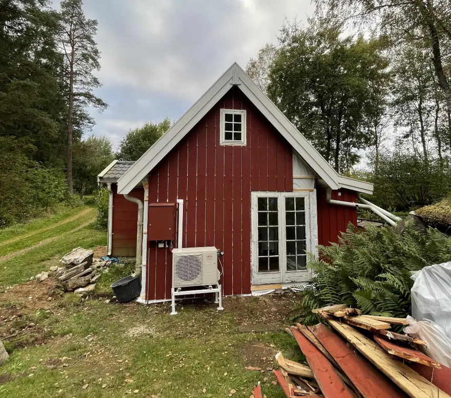 Rött sommarhus i Skånes Värsjö under pågående fasadarbete med nymonterad lockpanel och vita vindskivor
