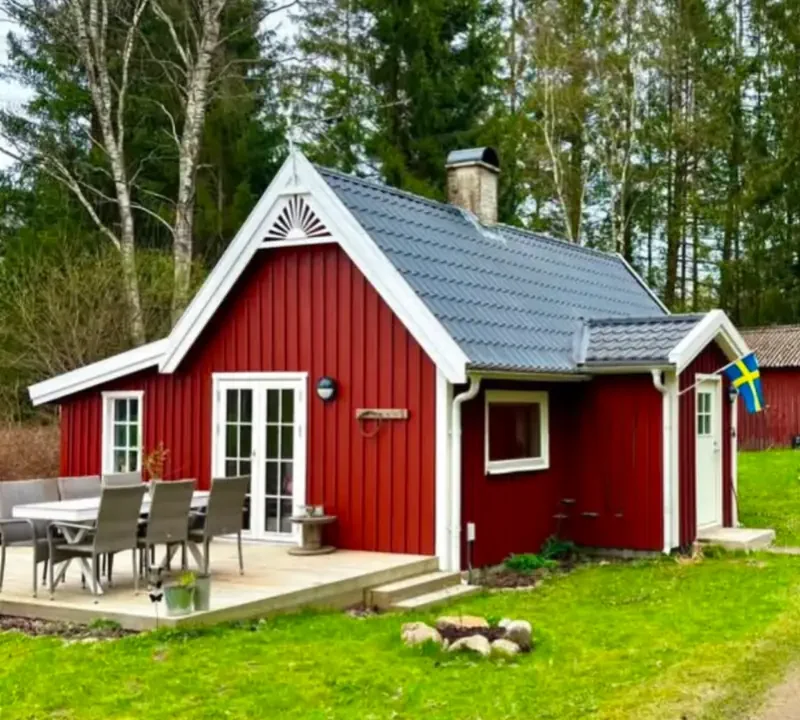 Falurött sommarhus i Skånes Värsjö med vita knutar, vindskivor och en soluppgång i trä på gaveln