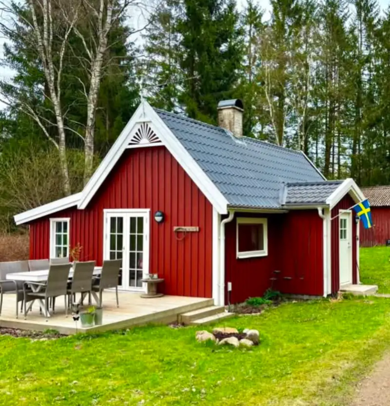 Falurött sommarhus i Skånes Värsjö med vita knutar, vindskivor och en soluppgång i trä på gaveln