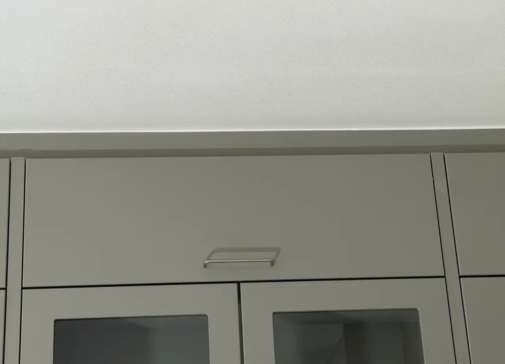 Närbild på den raka skarven mellan gröngråa köksöverskåp och färdigspacklat vitt tak i Höllviken