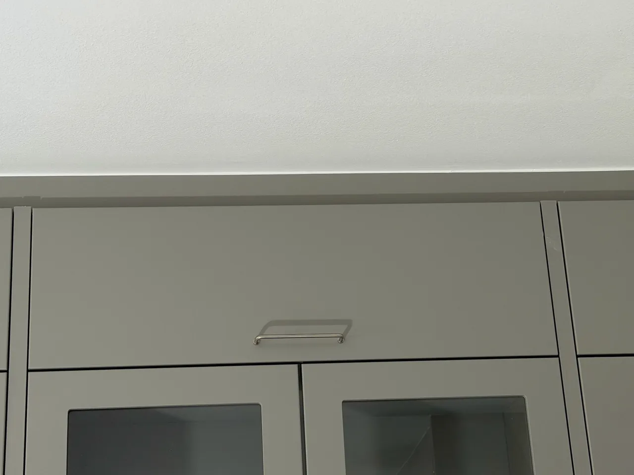 Närbild på den raka skarven mellan gröngråa köksöverskåp och färdigspacklat vitt tak i Höllviken